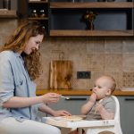 A mother lovingly feeds her baby in a modern kitchen. Heartwarming family moment.