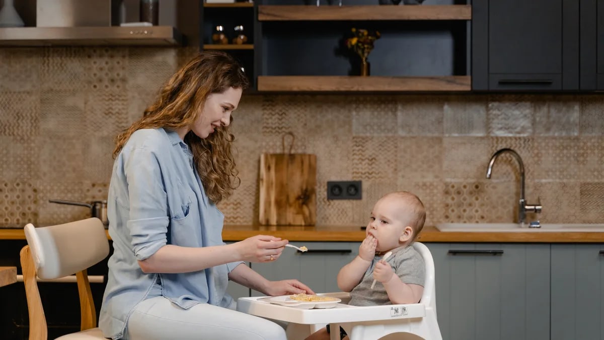 A mother lovingly feeds her baby in a modern kitchen. Heartwarming family moment.